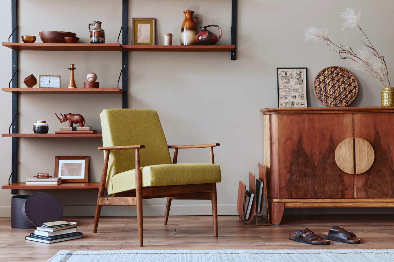 Stylish composition of retro living room interior with design armchair, wooden bookcase, picture frames, plant, carpet, slippers, decoration and elegant accessories in home décor.
