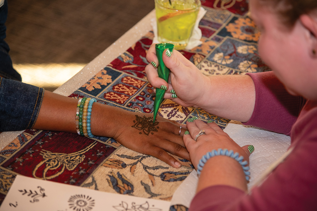 woman making henna pattern on woman's hand